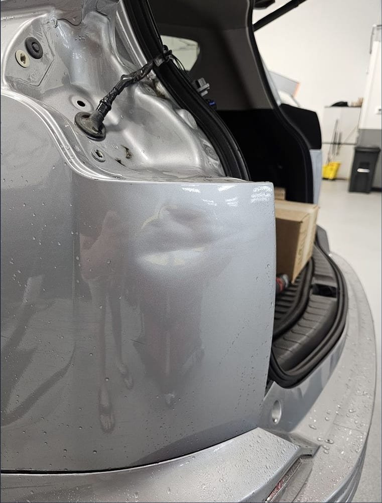 Dented rear quarter panel before repair, near the liftgate hinge